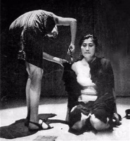 女子跪坐在地上，面前放着一把剪刀，和观众说：你们可以随便剪我的衣服