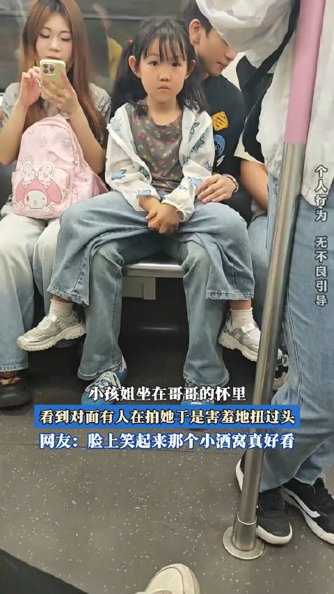 小孩姐坐在哥哥的怀里,看到对面有人在拍她于是害羞地扭过头