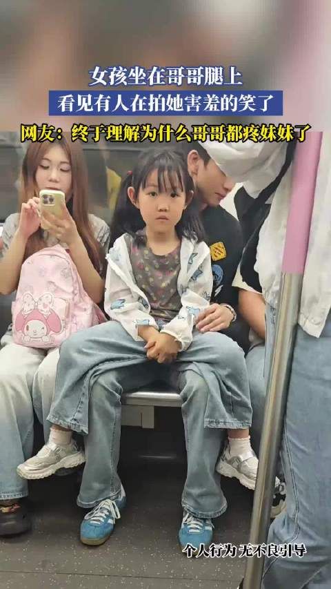 女孩坐在哥哥腿上,看见有人在拍她害羞的笑了
