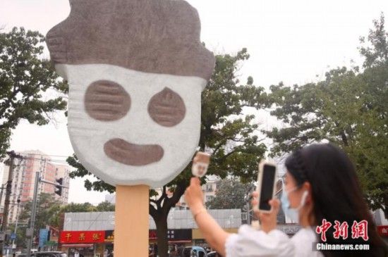 资料图：北京朝阳区街头摆放的雪糕装置布景吸引市民。图为市民拿着同款雪糕拍照留念。 中新社记者 易海菲 摄