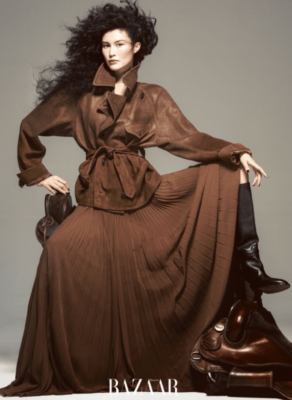 何穗棕调风衣搭同色系长裙，单手轻掀裙摆的姿态灵动优雅。