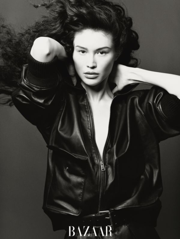 何穗黑皮外套造型，抬手轻抵颈肩的姿态慵懒松弛。