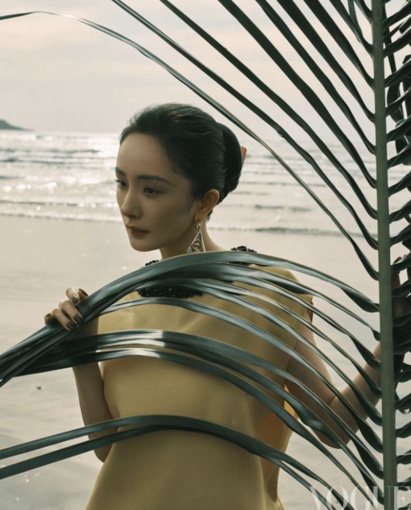 杨幂手持棕榈叶轻遮身侧，暖调造型衬得气色柔和。