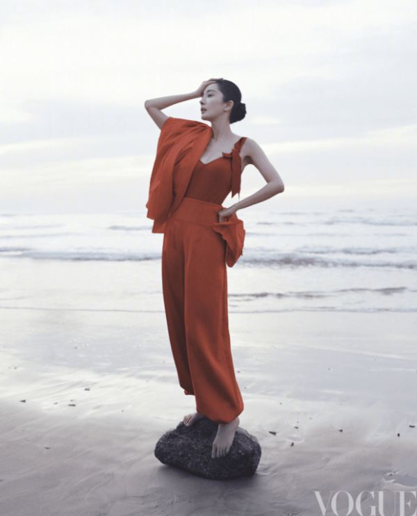 杨幂身着红装立于海边，抬手轻抵脖颈的姿态利落明艳。