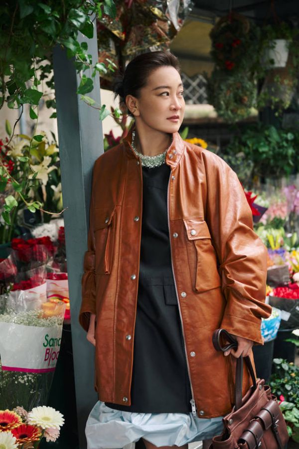 贾玲驻足石墙前，棕皮衣穿搭简约又时髦。