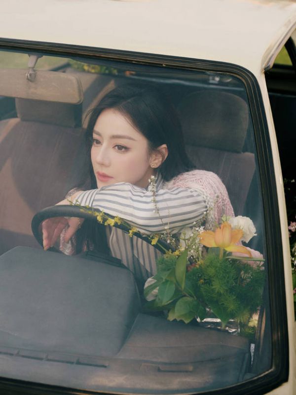 迪丽热巴手搭方向盘,身旁鲜花环绕,眼神温柔,治愈浪漫。